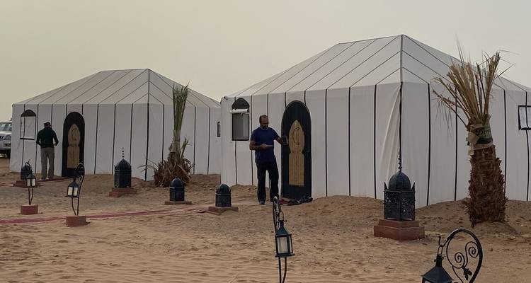 Des tentes de style berbère blanc installées sur un terrain sablonneux au crépuscule