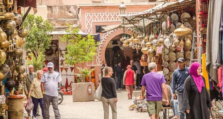 Rue du souk animée bordée de lampes, de poteries et de clients dans la médina de Marrakech