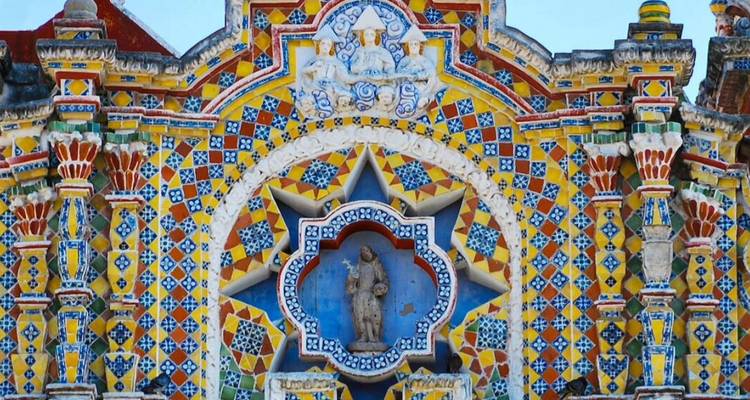 Nahaufnahme einer aufwändig gekachelten barocken Kirchenfassade mit lebendigen gelben, blauen und roten Mustern um eine kleine Heiligenstatue.