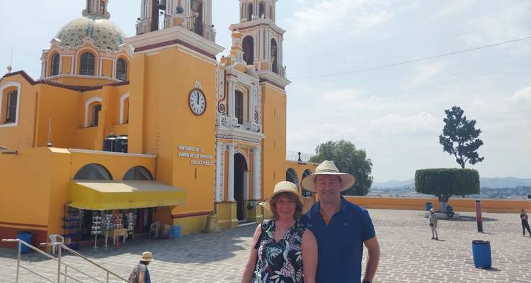 Touristen mit Hüten, die vor einer hell gelben historischen Kirche mit zwei Glockentürmen und einer Uhr in Puebla posieren.