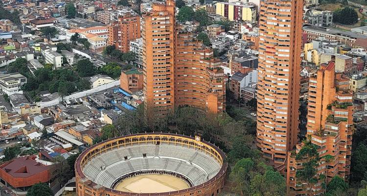 Vue aérienne d'une arène circulaire entourée de grands immeubles d'appartements de couleur orange dans une zone urbaine densément peuplée.