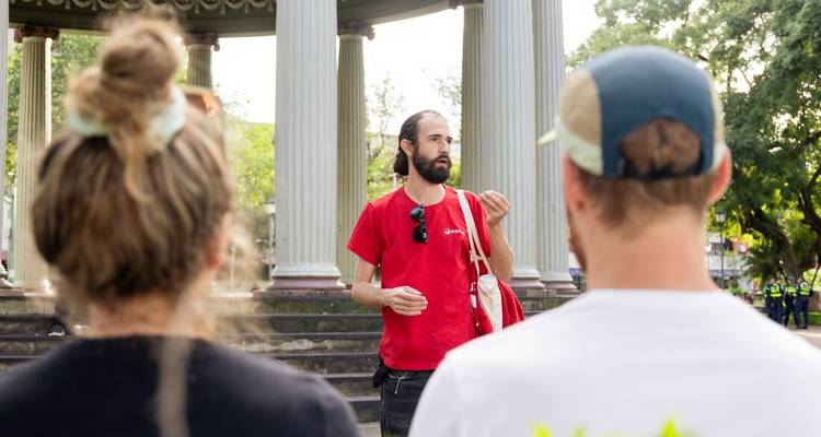 A guide in a red shirt leads a small group during a city walking tour beside classical columns.