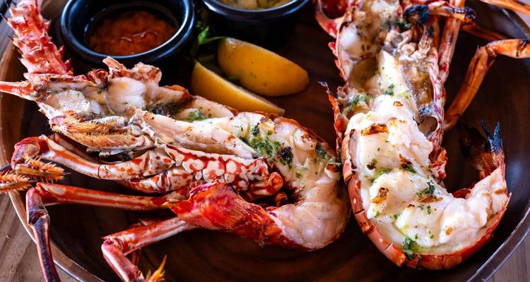 Grilled lobster halves served with lemon wedges and dipping sauces on a rustic plate.