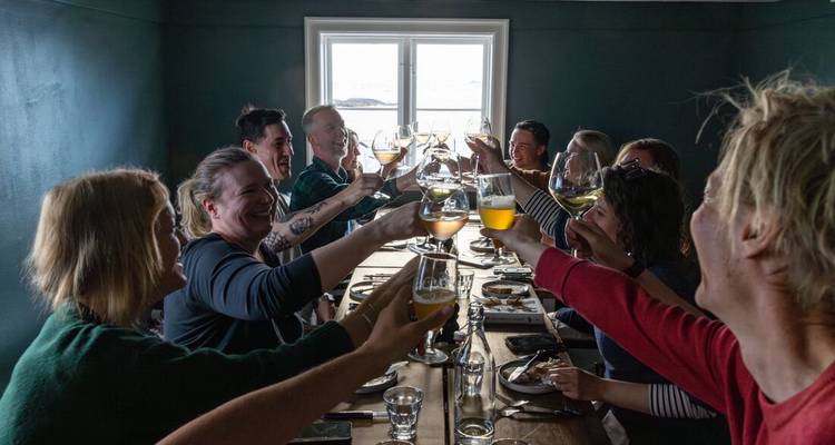 A cheerful group clinks glasses around a long dining table beside a bright window.