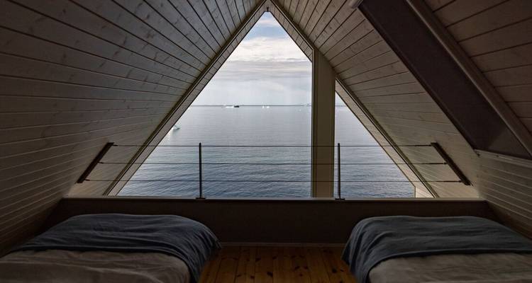 An A-frame loft bedroom with twin beds overlooks a serene Arctic sea through a triangular window.