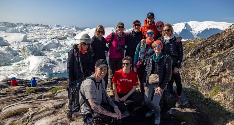 A hiking group poses on rocky terrain with a vast broken-ice glacier behind them.