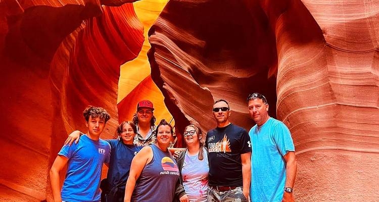 Een groep reizigers glimlacht voor een foto in de gloeiende oranje bochten van Antelope Canyon.