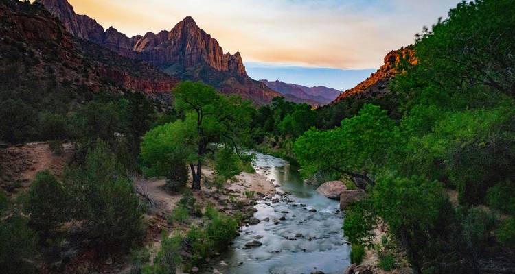 Rivier die onder rode zandsteenpiekenen in Zion National Park bij schemering kronkelt met zachte avondkleuren.