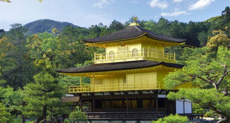 El Pabellón Dorado (Kinkaku-ji) brilla intensamente rodeado de vegetación exuberante y cielo azul en Kyoto.