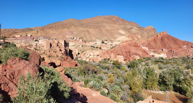 Los acantilados rojos y ocres se elevan sobre un pueblo marroquí tradicional y un valle verde