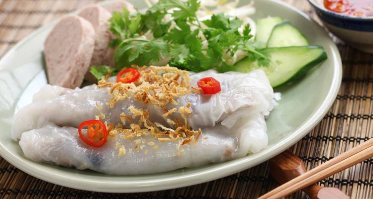 Vietnamesischer Teller mit durchsichtigen Reisnudeln, belegt mit gebratenen Schalotten und Chili, mit Kräutern und Gurke als Beilage.