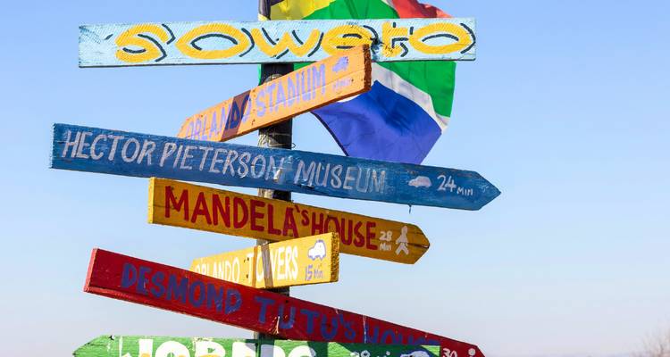 Kleurrijke houten wegwijzer in Soweto die naar lokale bezienswaardigheden wijst tegen een heldere blauwe hemel.
