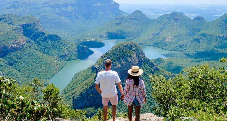 Een stel dat elkaar vasthoudt bewondert de uitgestrekte groene rotsen en slingerende blauwe rivier van de Blyde River Canyon vanaf een hoog uitkijkpunt.