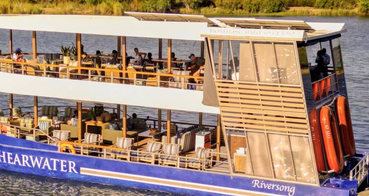 Tweeverdiepigsightseeing-boot die een brede rivier afvaart met zittende passagiers die van het uitzicht genieten.