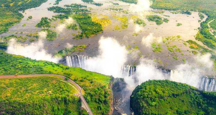 Spectaculair luchtfoto van Victoria Falls met mistpluimen die boven smaragdgroene riverkloven omhoog stijgen.