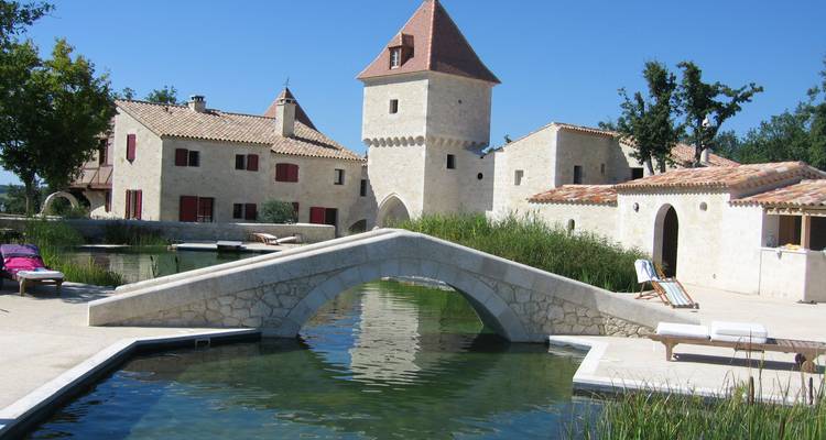 Stone manor complex with tower and arched bridge spanning a tranquil pool