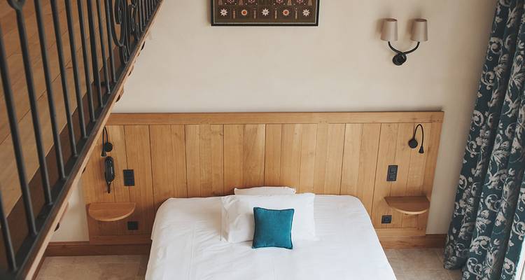 Simple hotel bedroom with wooden headboard, teal accent pillow and loft railing overhead