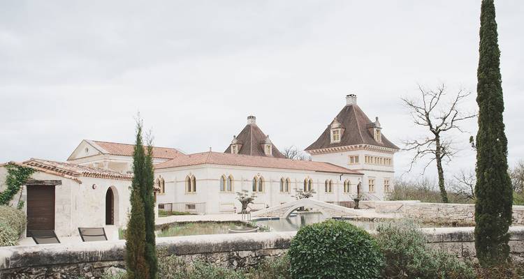 Exterior view of elegant French estate with tall cypress trees and cloudy sky