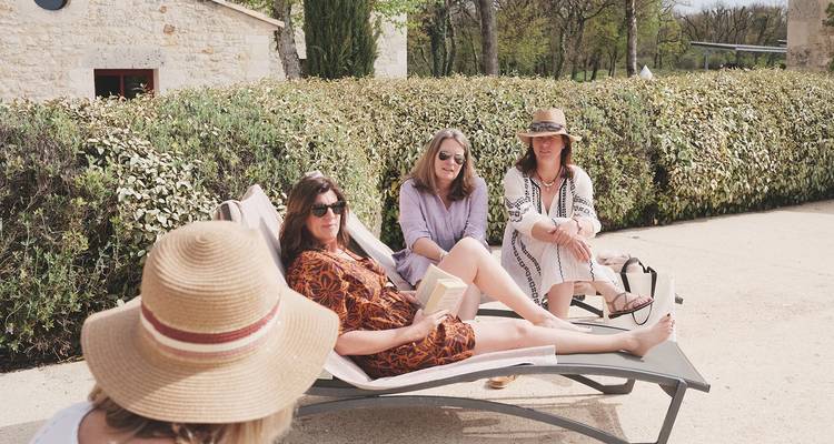 Mujeres relajándose en tumbonas junto a un seto disfrutando de un día soleado.