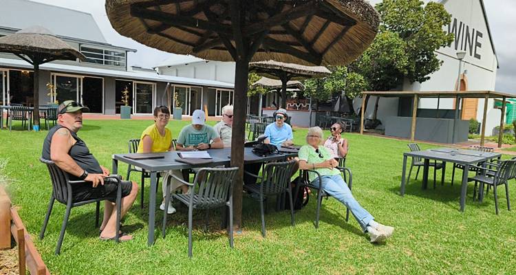 Les voyageurs se détendent sous un parasol en chaume sur les pelouses verdoyantes à l'extérieur d'un bâtiment de vignoble.
