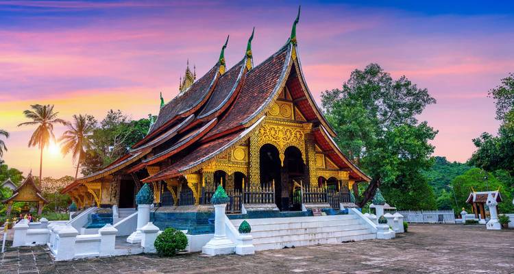 Der exquisit verzierte Wat Xieng Thong Tempel in Luang Prabang, leuchtend in einem farbenfrohen Sonnenuntergang.
