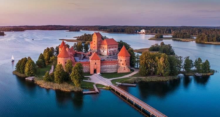Vue aérienne romantique du château de l'île de Trakai entouré par les eaux calmes du lac au crépuscule.