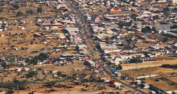 Vue aérienne d'une vaste foire désertique remplie de tentes, d'étals, de bétail et de foules s'alignant le long d'une route centrale poussiéreuse.
