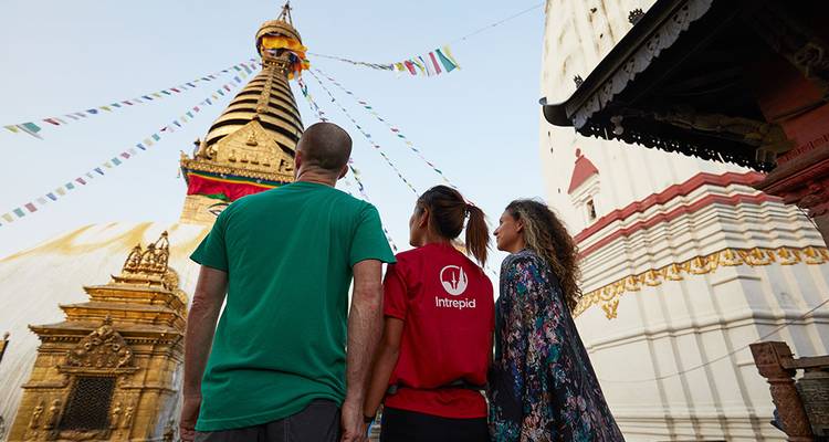 Los viajeros alzan la vista hacia la Estupa de Swayambhunath en Katmandú adornada con banderas de oración coloridas.