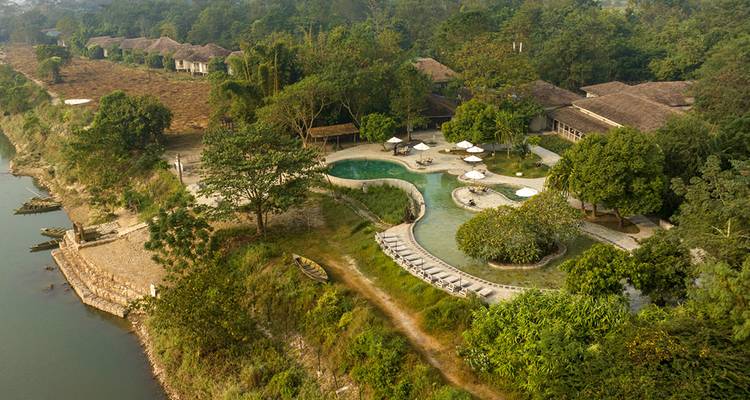 Vista aérea de un complejo de eco-lodge con piscinas de forma libre ubicadas en la densa selva ribereña de Chitwan.