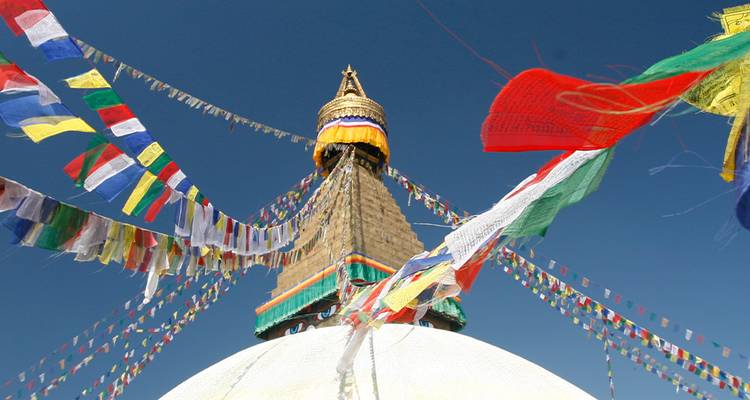 Gebedsvlaggen wapperen rond de witte koepel en gouden spits van de Boudhanath Stupa tegen een heldere blauwe lucht.