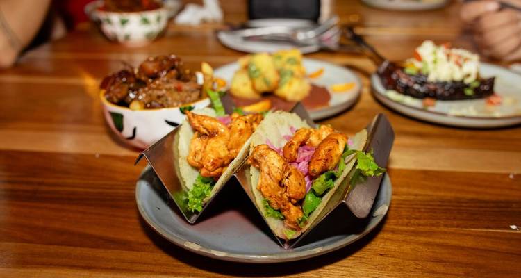 Plate of flavorful chicken tacos garnished with lettuce and pickled onions on a wooden restaurant table.