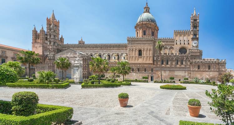 De sierlijke gevel en koepel van de Kathedraal van Palermo domineren een zonnig binnenplein met keurig verzorgde hagen.