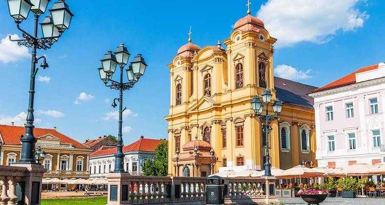Baroque yellow cathedral dominates a sunny square lined with pastel buildings and ornate street lamps.