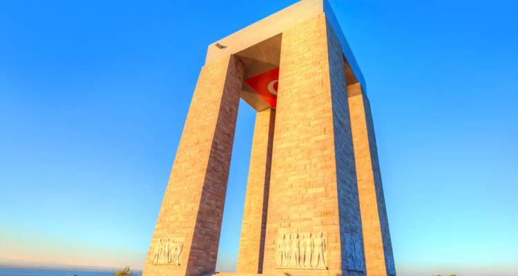 Massief stenen gedenkteken in de vorm van een boog die hoog boven je uittorent tegen een strakblauwe hemel, met gesneden reliëfsoldaten aan de voet.