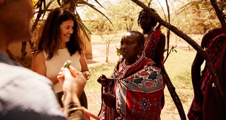 Reiziger luistert naar een Maasai-oudere onder schaduwrijke bomen tijdens een boeiende culturele uitwisseling.
