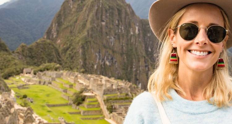 Voyageur souriant portant des lunettes de soleil pose avec les ruines emblématiques du Machu Picchu et les montagnes en arrière-plan.