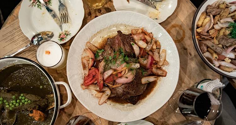Vue de dessus d'une assiette de lomo saltado garnie d'herbes aromatiques entourée de boissons et de plats d'accompagnement.