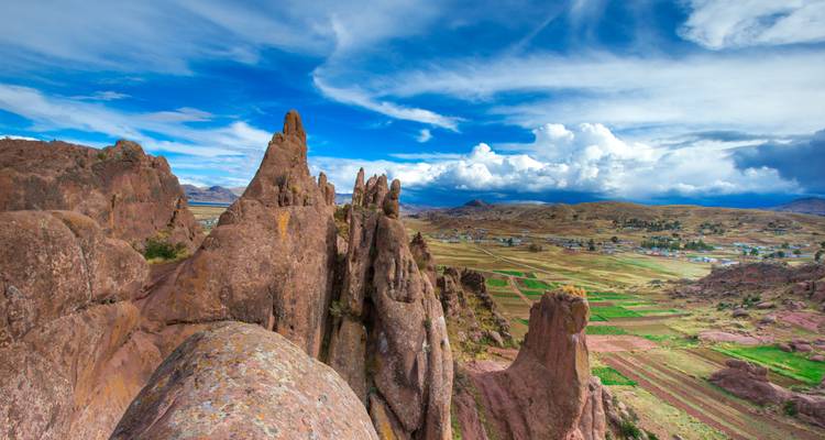 Formaciones de roca roja irregular que se asoman a campos agrícolas de retazos bajo cielos dramáticos en las tierras altas de Perú.