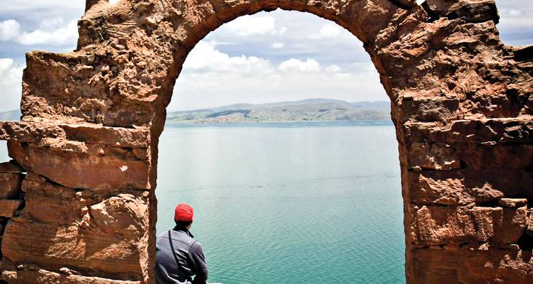 Viajero mirando las aguas azules del Lago Titicaca a través de un arco de piedra antiguo en la Isla de Taquile.