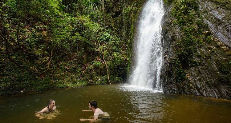 Deux nageurs profitent d'une piscine naturelle sous une cascade étroite de la forêt tropicale.