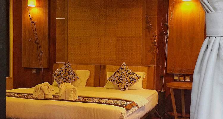 Chambre d'hôtel chaleureusement éclairée avec des oreillers à motifs, de l'art textile et une décoration en bois.