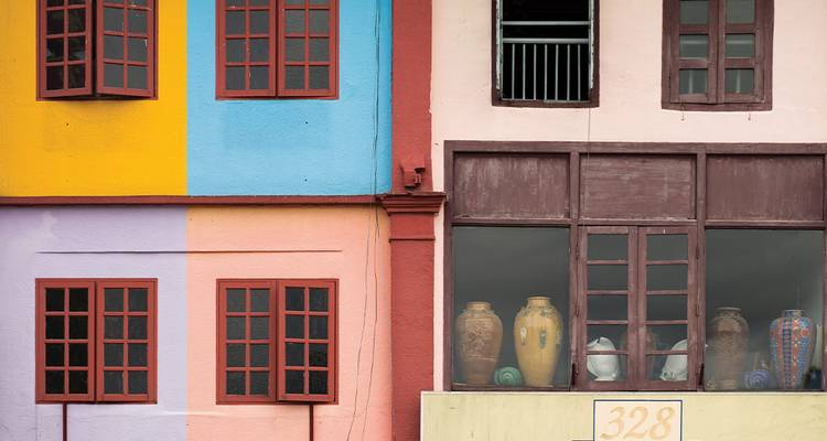 Façade colorée d'un bâtiment aux murs pastel, fenêtres en bois et pots en céramique exposés.