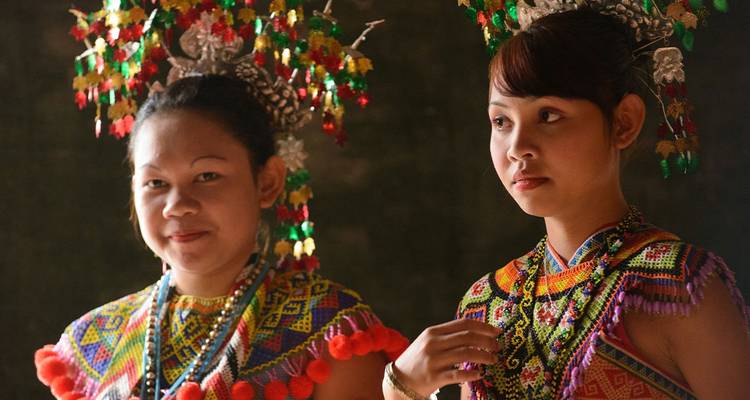 Deux femmes portent des coiffures et des vêtements traditionnels aux perles éclatantes dans une lumière intérieure douce.