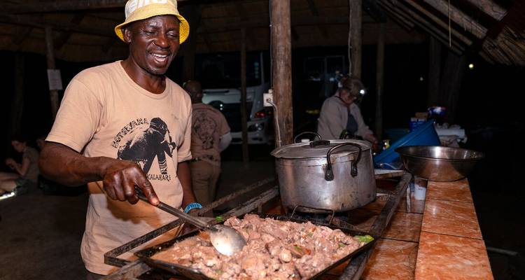 Un cuisinier jovial remue un grand plateau de ragoût dans une cuisine de camp en plein air la nuit.