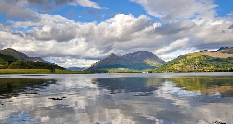 Les montagnes écossaises spectaculaires se reflètent sur les eaux calmes d'un large loch sous un ciel nuageux par endroits.