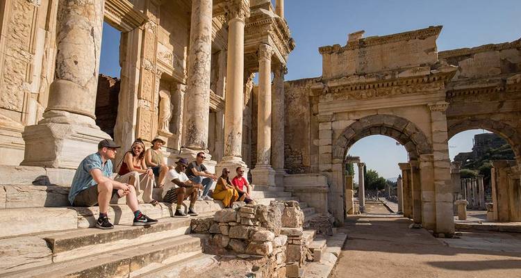 Les voyageurs se reposant sur les marches des ruines de l'ancienne Bibliothèque de Celsus sous un ciel dégagé.