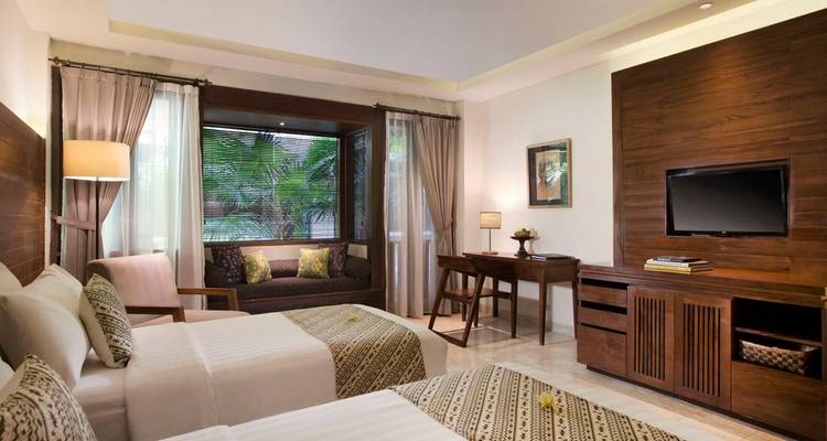Comfortabele hotelkamer met twee aparte bedden, groot raamzitje, houten inrichting en uitzicht op de tuin.