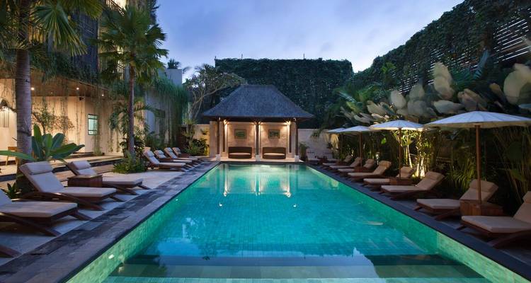 Elegant verlichte zwembadtuin van Balinese resort bij schemering met ligbedden en weelderige planten.