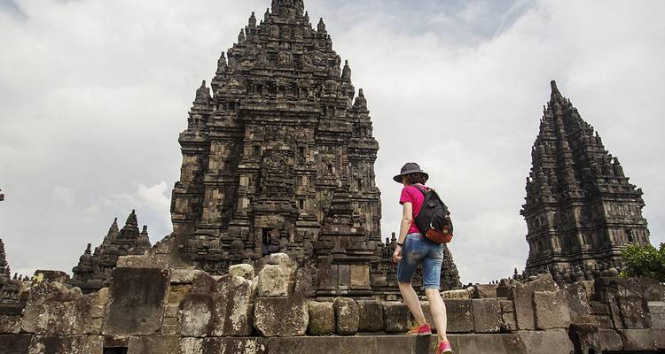 Vrouwelijke reiziger die naast de imposante stenen torens van het Prambanan Tempelcomplex loopt op een bewolkte dag.