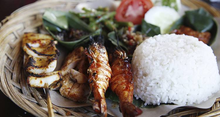 Close-up van een Indonesisch zeevruchtenplateau met gegrilde garnalen, inktvis en rijst op een geweven dienblad.